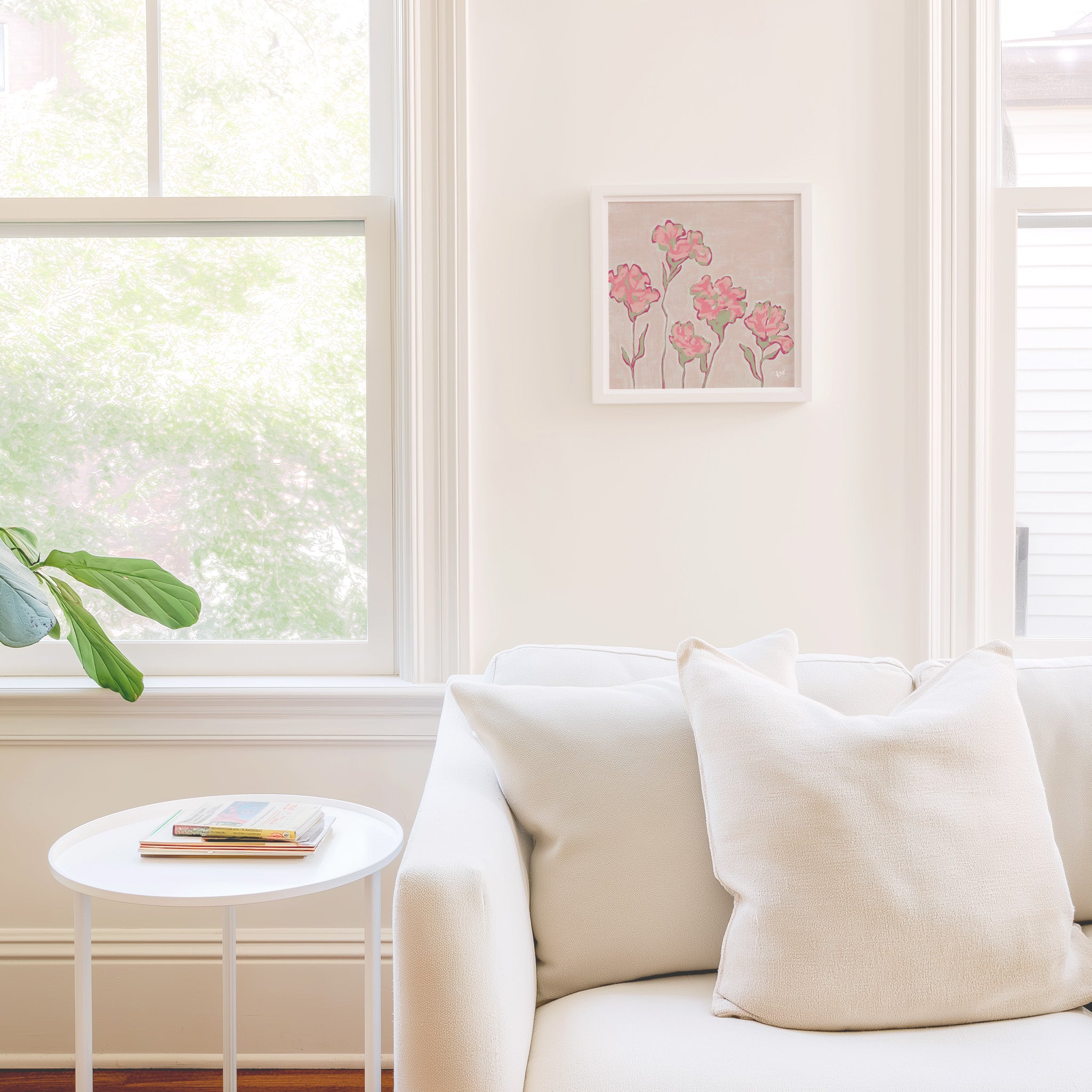 a cozy living room with a white sofa, a small round table, and a framed artwork featuring pink flowers on the wall.