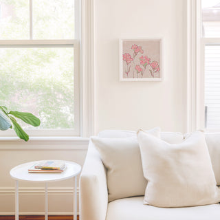 a cozy living room with a white sofa, a small round table, and a framed artwork featuring pink flowers on the wall.