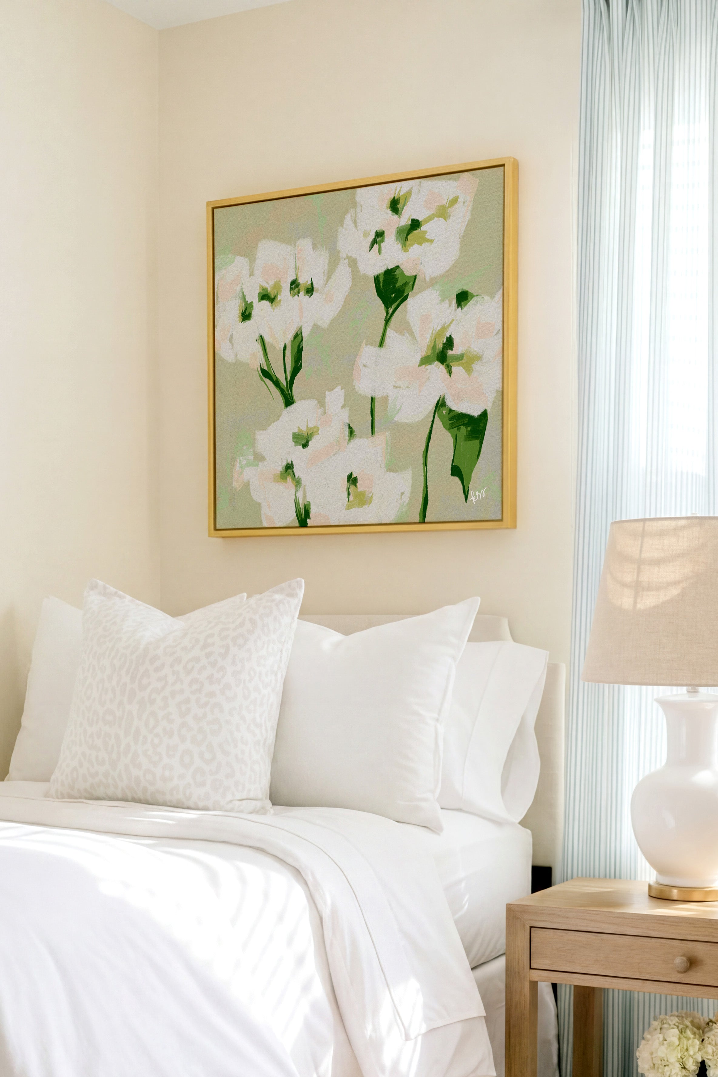 a serene bedroom scene with a bed adorned with white pillows and a white comforter, complemented by a framed floral artwork hanging above it.
