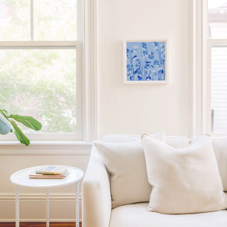 a cozy living room with a white sofa, a small white side table, and a framed blue floral artwork on the wall.