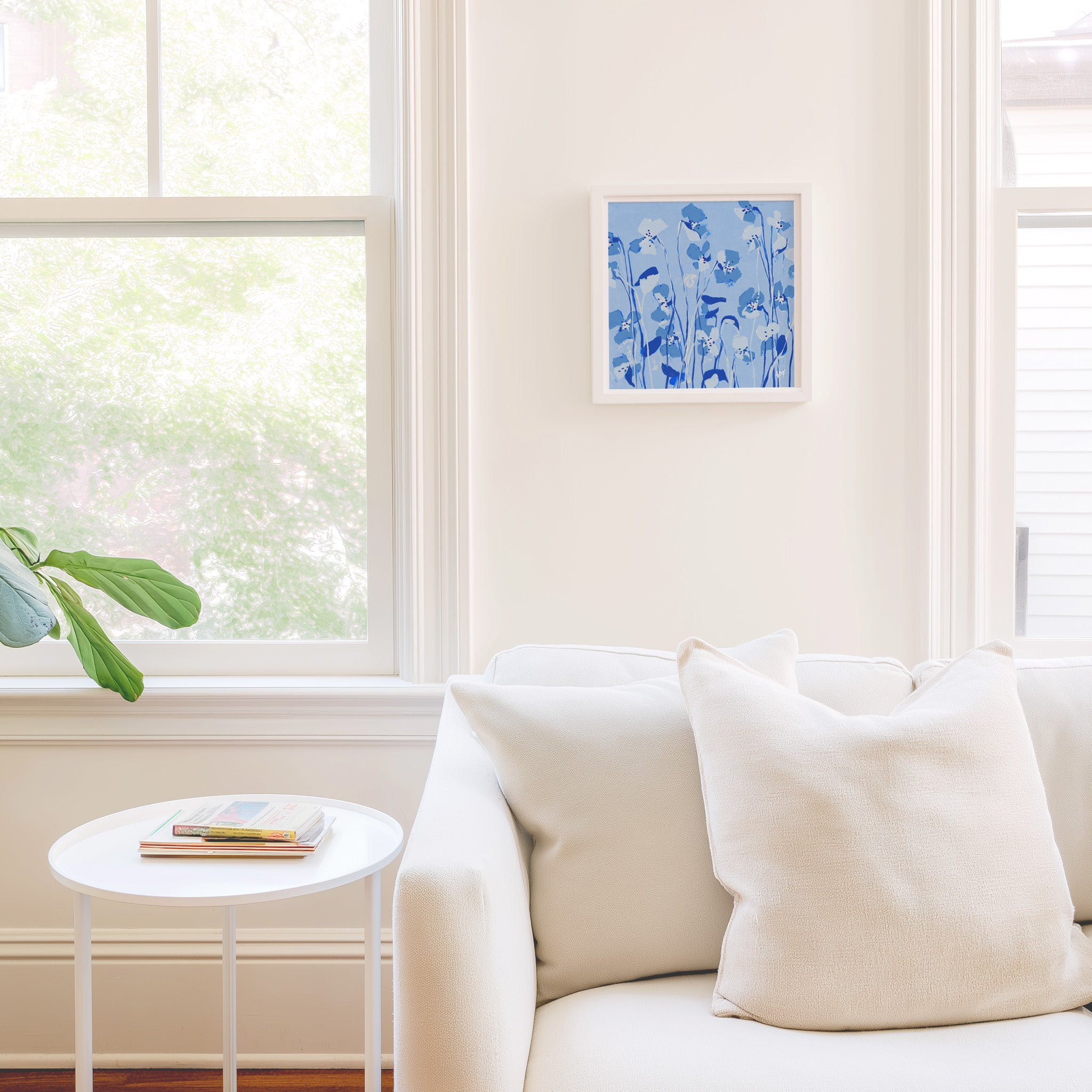a cozy living room with a white sofa, a small white side table, and a framed blue floral artwork on the wall.