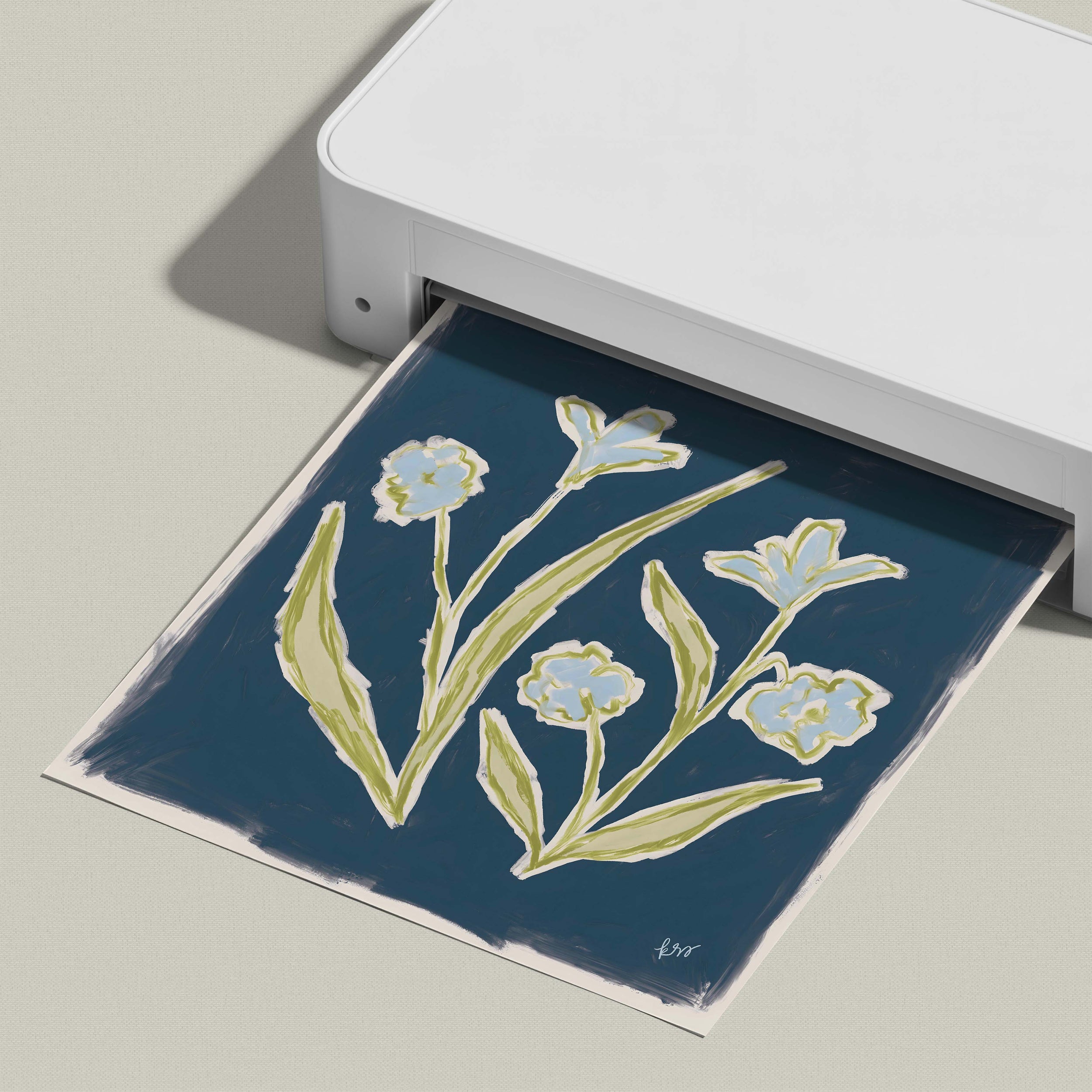 A white printer is displaying a printed image of a blue floral design on a dark background.