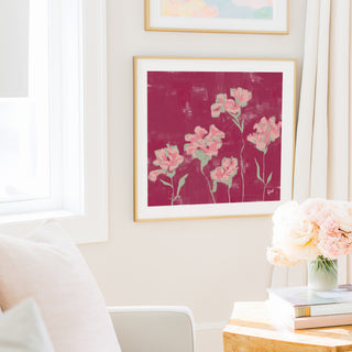 a cozy living room with a framed painting of pink flowers hanging on the wall, a vase of pink flowers on a table, and a bookshelf filled with books.