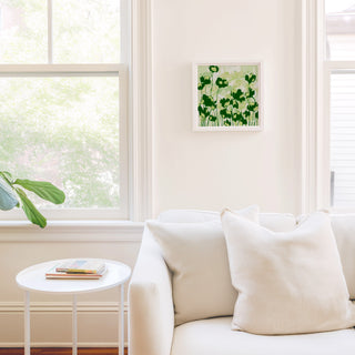 a cozy living room with a white sofa, a small round table, and a framed picture of green flowers on the wall.