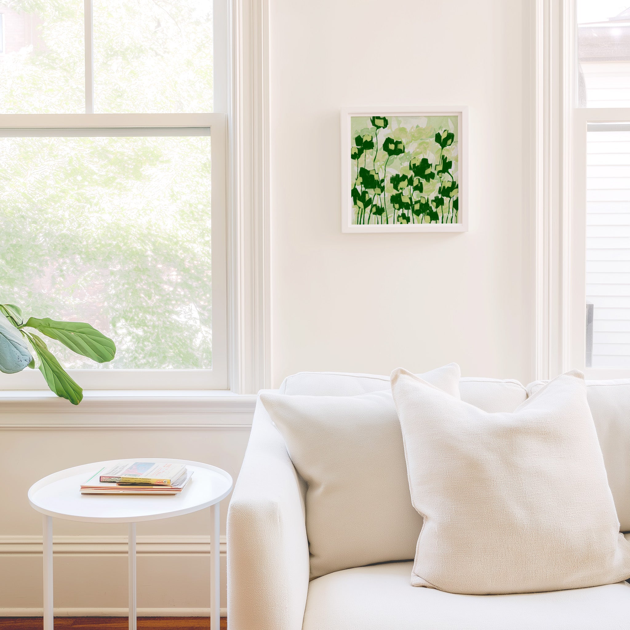 a cozy living room with a white sofa, a small round table, and a framed picture of green flowers on the wall.