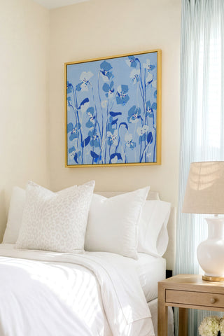a serene bedroom scene with a bed adorned with white linens and a framed blue floral artwork hanging above it.