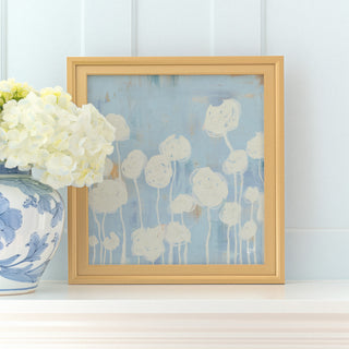 a framed artwork of white flowers on a white shelf, accompanied by a blue and white vase filled with white hydrangeas.