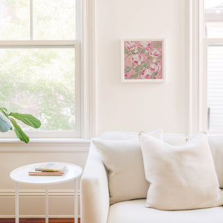 a cozy living room with a white sofa, a small round table, and a framed artwork of pink flowers hanging on the wall.