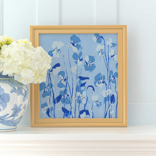 a framed painting of blue flowers on a white shelf, with a vase of white hydrangeas placed next to it.