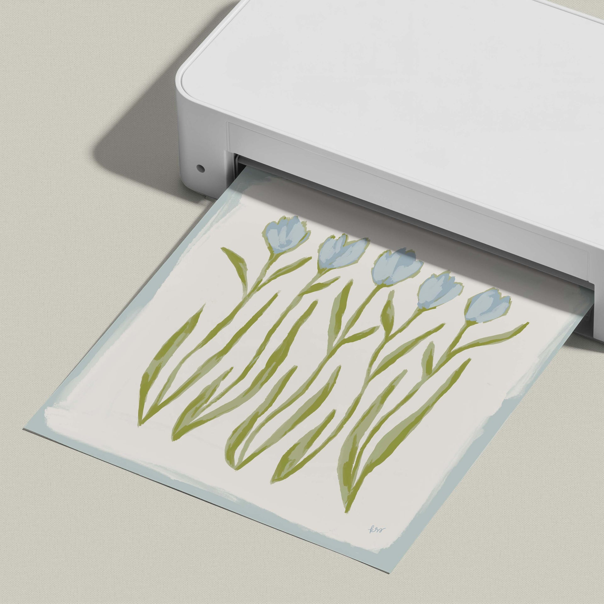 A white printer is printing a paper with a design of blue flowers on it.