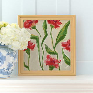 a framed painting of red flowers with green leaves, placed on a white shelf next to a blue and white vase with white flowers.