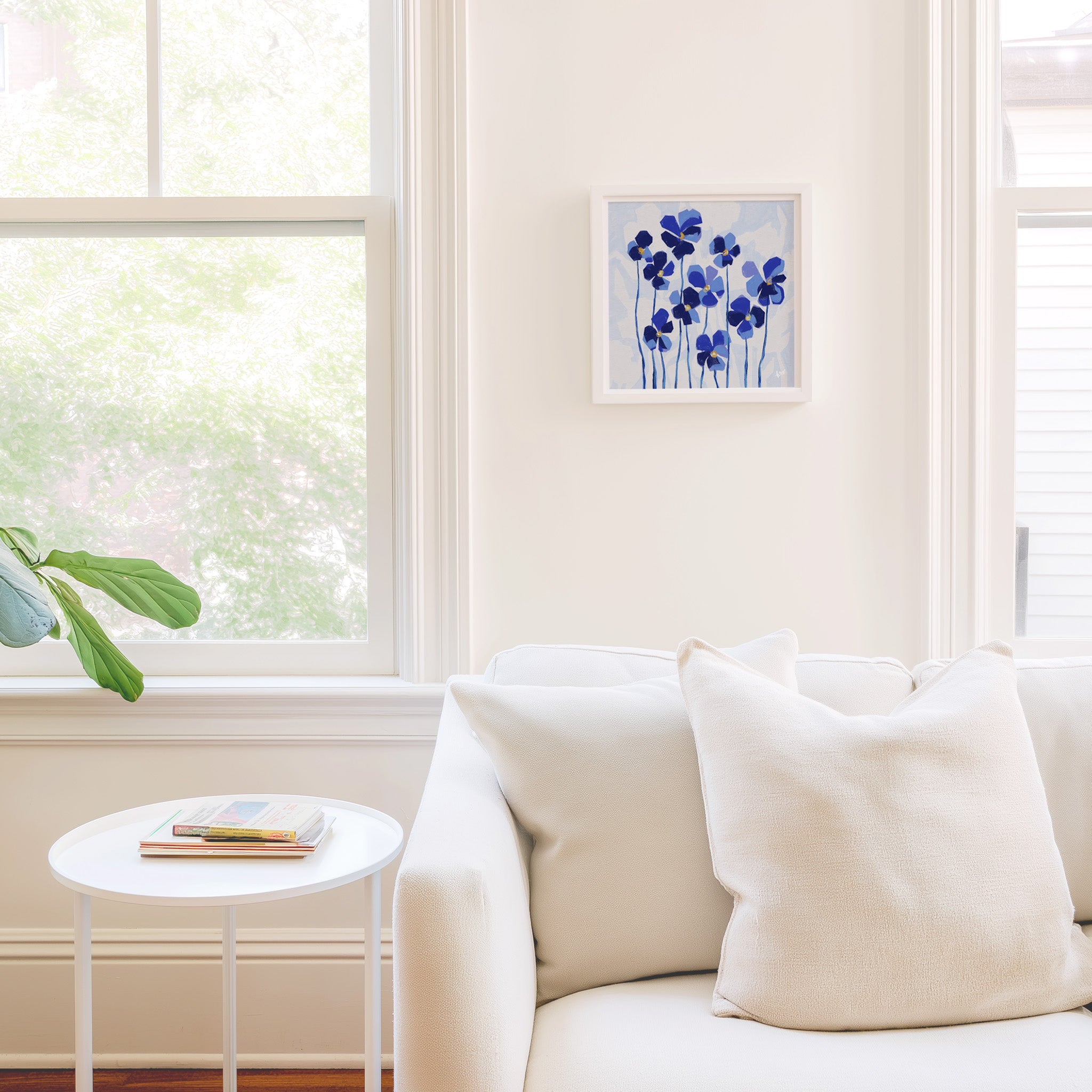 a cozy living room with a white sofa, a small round table, and a framed artwork of blue flowers on the wall.