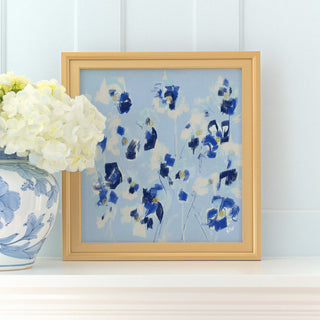 a framed painting of blue flowers on a white shelf, with a vase of white hydrangeas placed next to it.