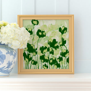 a framed painting of green and white flowers on a white shelf, with a vase of white hydrangeas placed next to it.