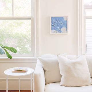 a cozy living room with a white sofa, a small white side table, and a framed artwork of blue flowers hanging on the wall.