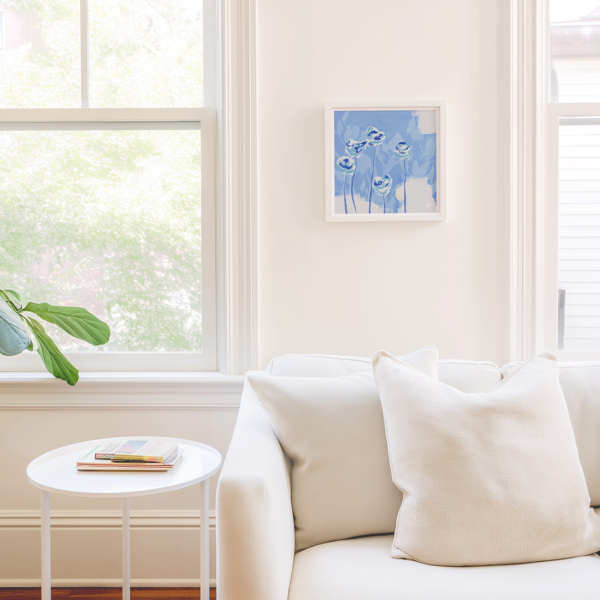 a cozy living room with a white sofa, a small white side table, and a framed artwork of blue flowers hanging on the wall.