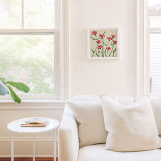 a cozy living room with a white sofa, a small round table, and a framed artwork of red flowers on the wall.