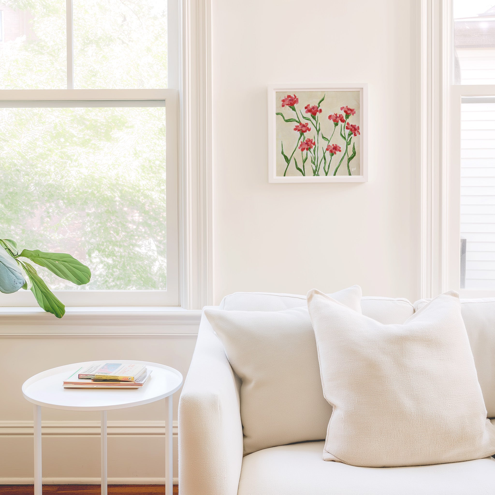 a cozy living room with a white sofa, a small round table, and a framed artwork of red flowers on the wall.
