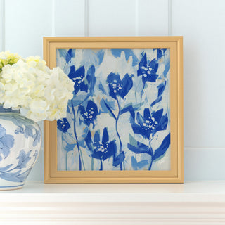 a framed painting of blue flowers on a white shelf, with a vase of white hydrangeas placed next to it.