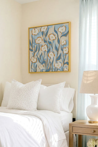 a serene bedroom scene with a bed adorned with white pillows and a white comforter, complemented by a framed floral artwork hanging above it.