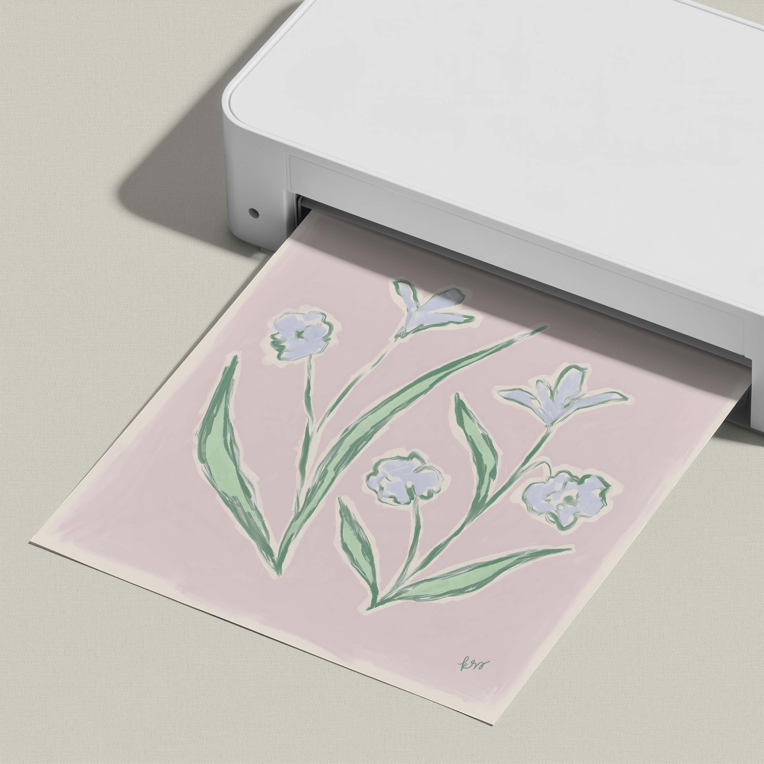 A white printer is printing a pink paper with a floral design featuring green leaves and blue flowers.