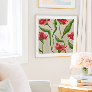 a cozy living room with a framed painting of red flowers hanging on the wall, a vase of pink flowers on a table, and a bookshelf filled with books.