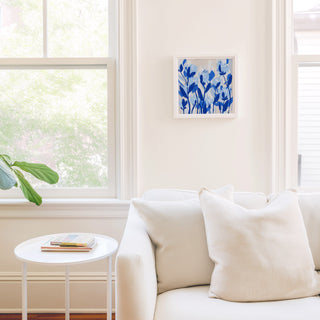 a cozy living room with a white sofa, a small white side table, and a framed blue floral artwork on the wall.