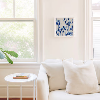 a cozy living room with a white sofa, a small round table, and a framed artwork featuring blue flowers on the wall.