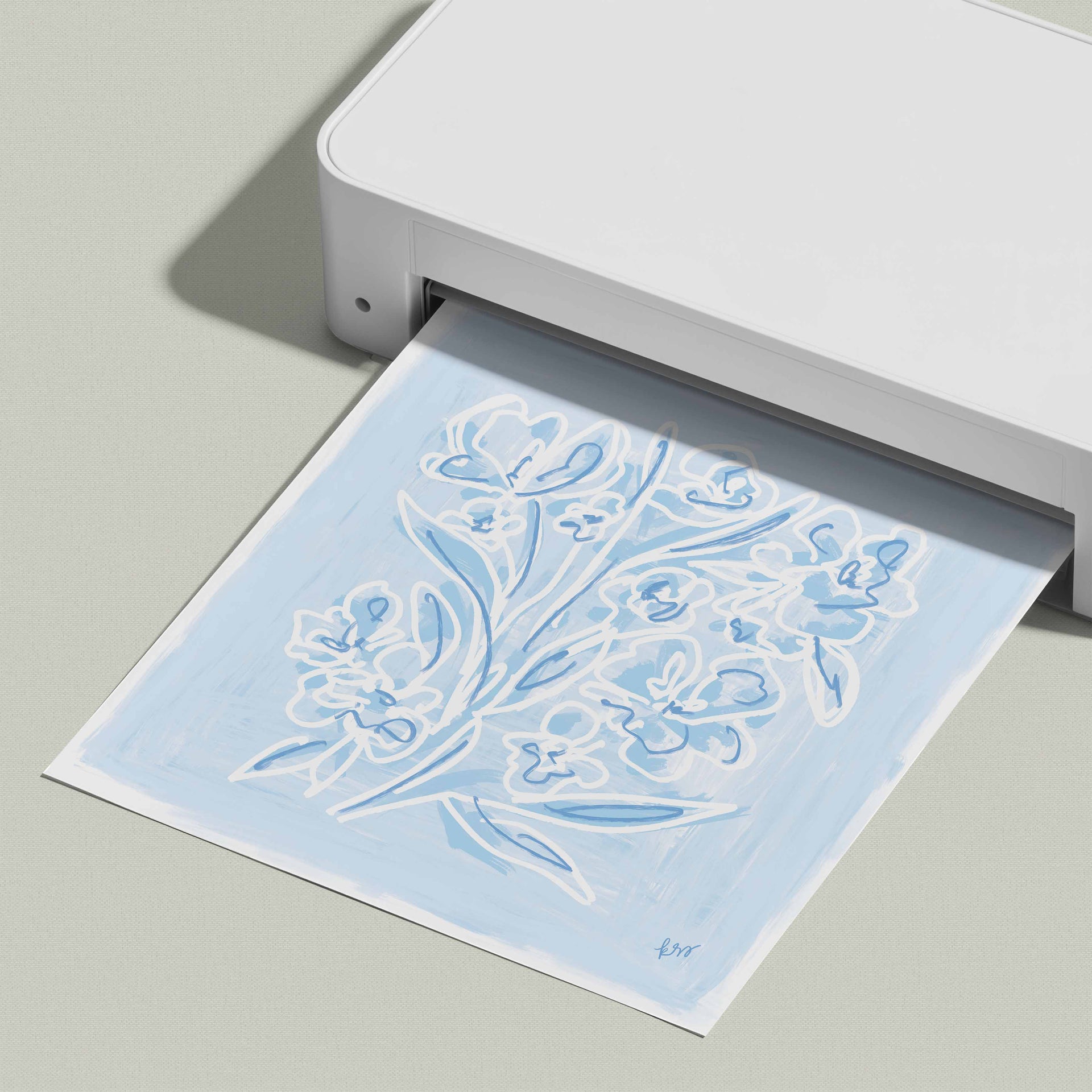 A white printer is printing a blue and white floral design on a piece of paper.