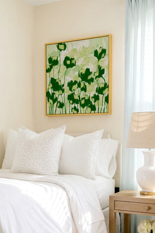 a serene bedroom scene with a bed adorned with white linens and a framed artwork featuring green flowers hanging above it.