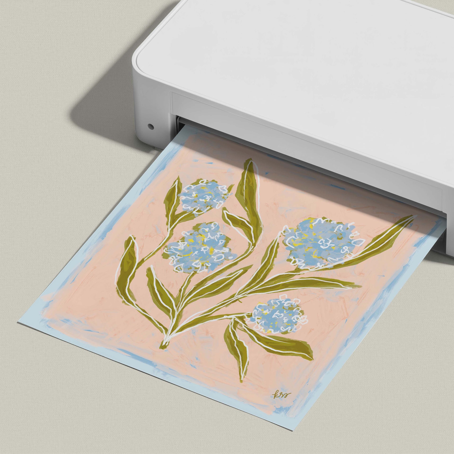 A white printer is printing a paper with a floral design featuring blue flowers and green leaves.