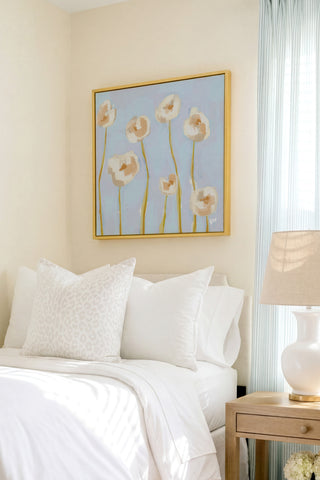 a serene bedroom scene with a bed adorned with white pillows and a white comforter, complemented by a framed painting of white flowers hanging above it. The room is further enhanced by a wooden nightstand and a lamp, creating a cozy and inviting atmosphere.