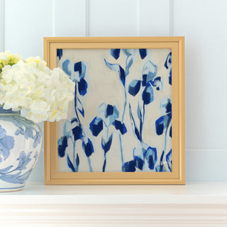 a framed painting of blue and white flowers on a white shelf, with a vase of white hydrangeas placed next to it.