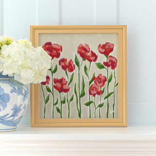 a framed painting of red flowers with green leaves, placed on a white shelf next to a blue and white vase with white flowers.