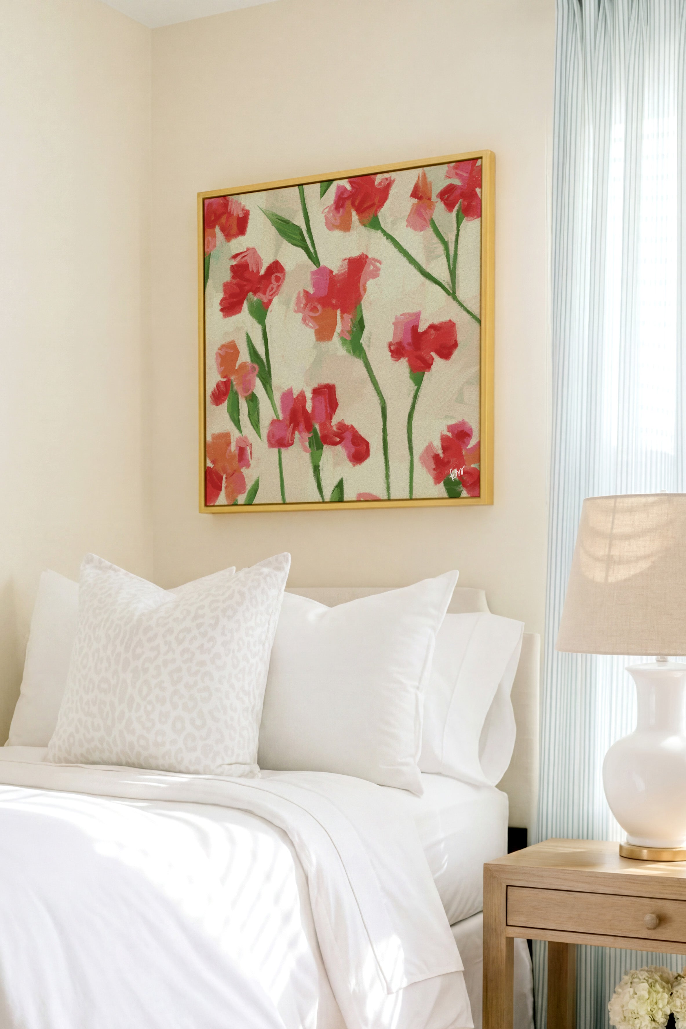 a cozy bedroom with a bed adorned with white pillows and a floral print bedspread. Above the bed, a framed painting of red flowers hangs on the wall, adding a touch of color and life to the room.