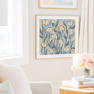 a cozy living room with a white sofa, a framed floral artwork on the wall, and a vase of pink flowers on a wooden table.