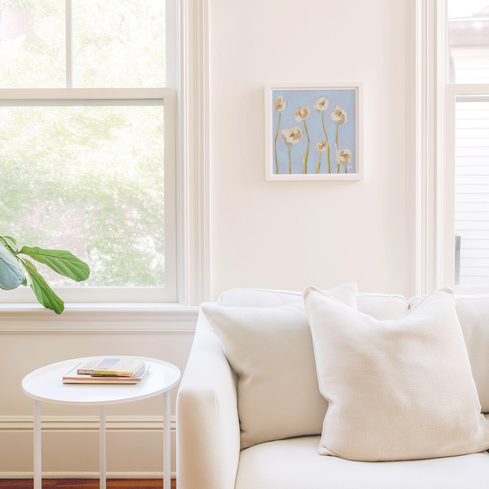 a cozy living room with a white sofa, a small round table, and a framed artwork of flowers on the wall.