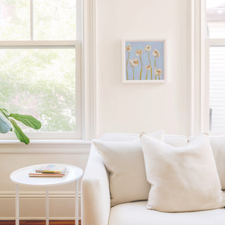 a cozy living room with a white sofa, a small round table, and a framed artwork of flowers on the wall.