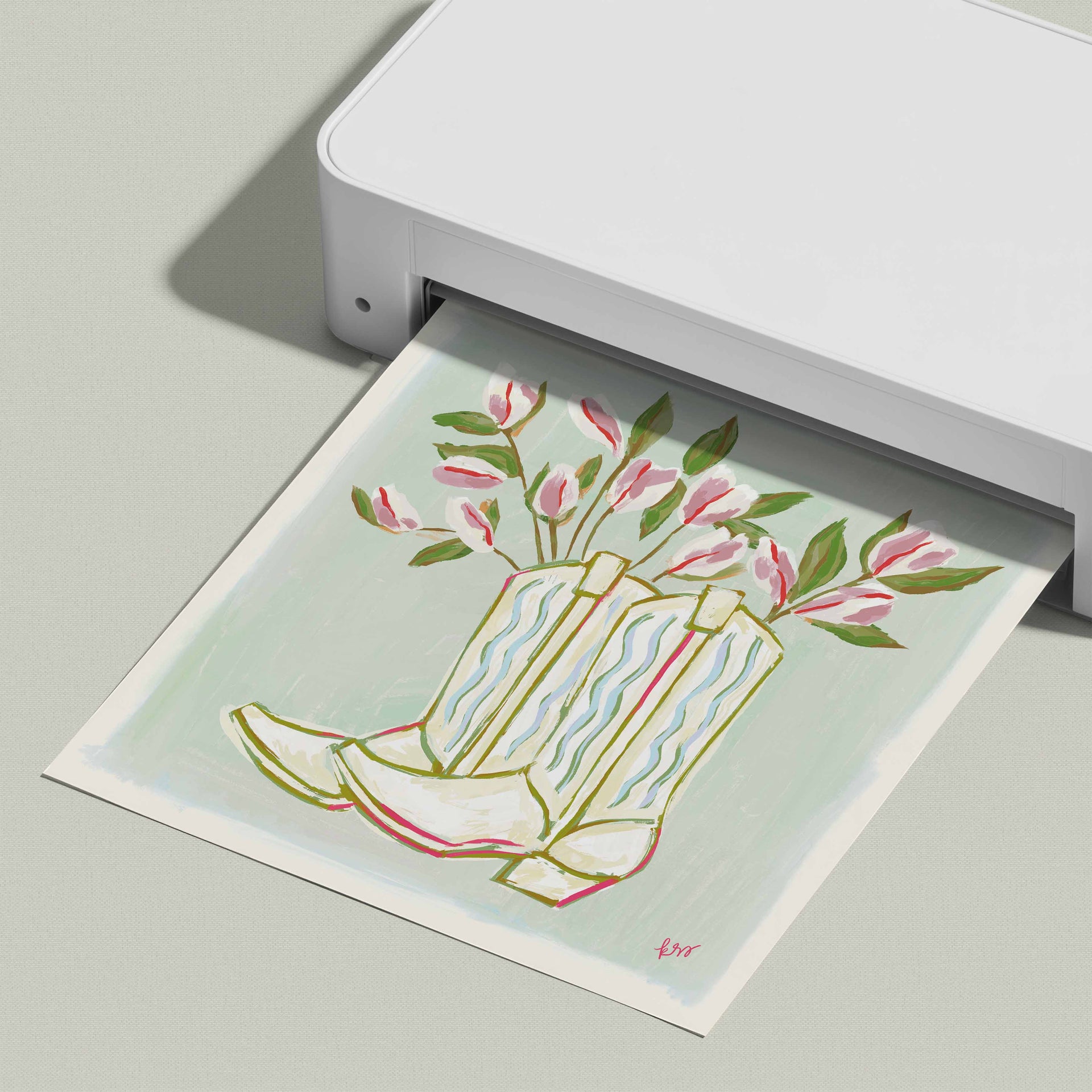 A white printer is printing a colorful illustration of a pair of white cowboy boots with pink flowers on a light green background.