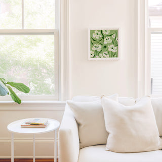 a cozy living room with a white sofa, a small round table, and a framed picture of white flowers hanging on the wall.