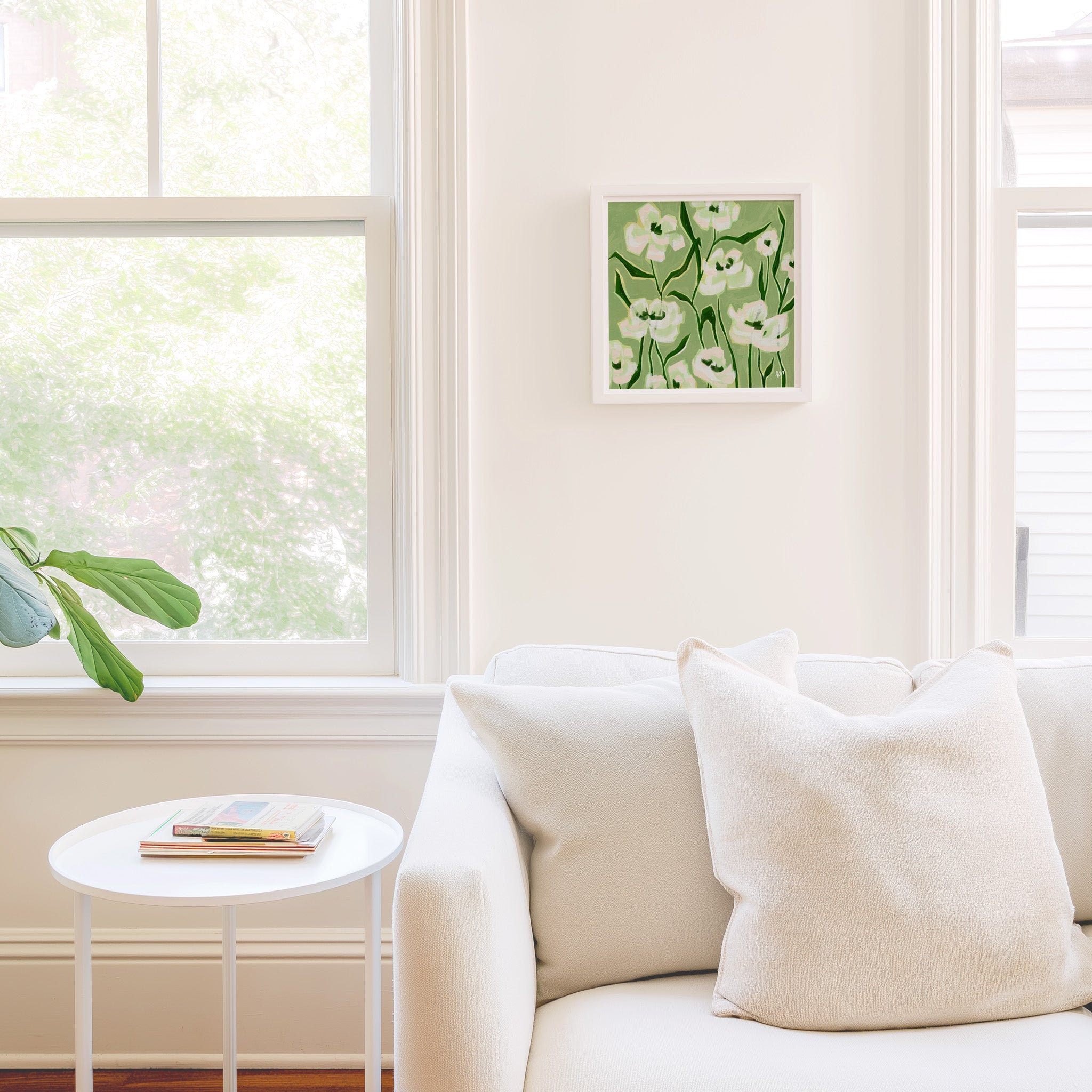 a cozy living room with a white sofa, a small round table, and a framed picture of white flowers hanging on the wall.