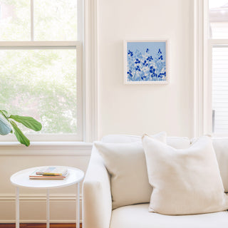 a cozy living room with a white sofa, a small round table, and a framed artwork of blue flowers on the wall.