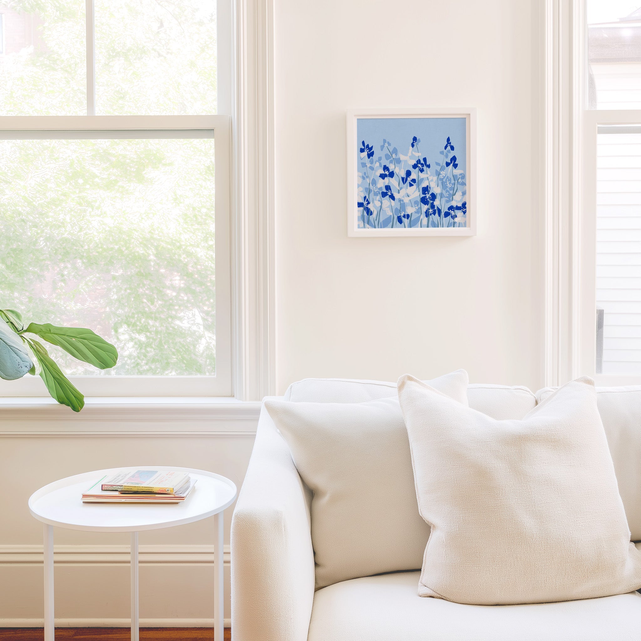 a cozy living room with a white sofa, a small round table, and a framed artwork of blue flowers on the wall.