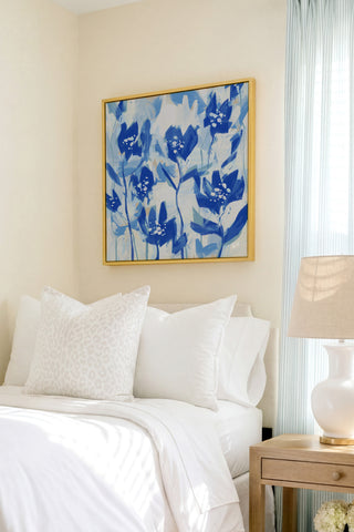 a serene bedroom scene with a bed adorned with white linens and a framed blue floral artwork hanging above it.