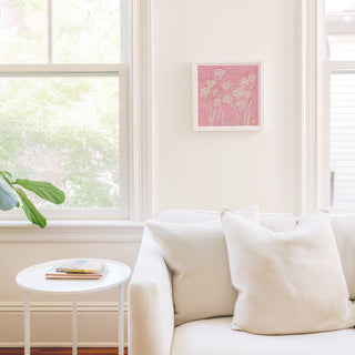 a cozy living room with a white sofa, a small round table, and a framed artwork of pink flowers on the wall.