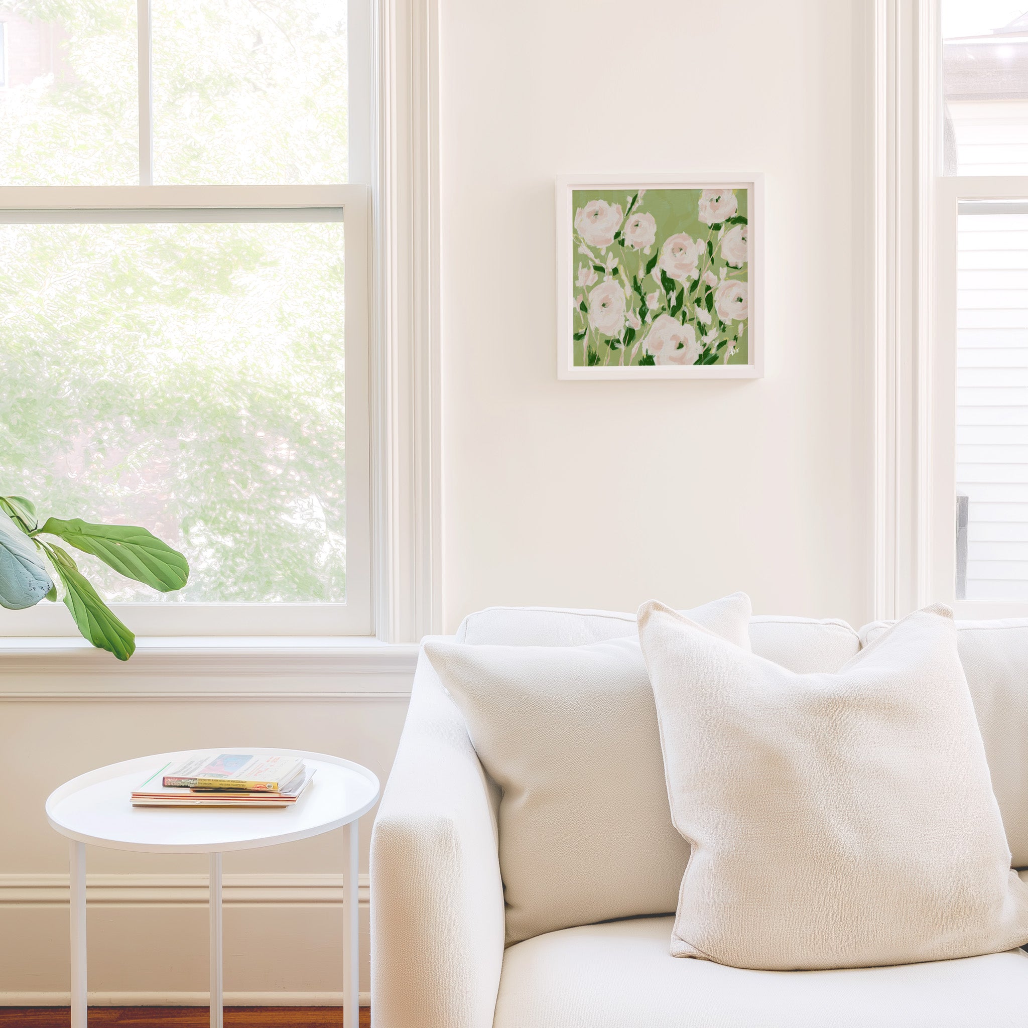 a cozy living room with a white sofa, a small round table, and a framed picture of flowers on the wall.