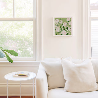 a cozy living room with a white sofa, a small round table, and a framed picture of flowers on the wall.