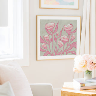 a cozy living room with a framed painting of pink flowers hanging on the wall, a vase of pink flowers on a table, and a bookshelf filled with books.