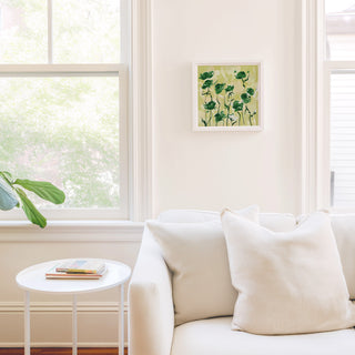 a cozy living room with a white sofa, a small round table, and a framed picture of green flowers on the wall.
