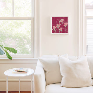 a cozy living room with a white sofa, a small round table, and a framed artwork featuring pink flowers on the wall.